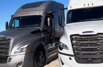 Two Freightliner trucks parked side-by-side, showing front and sides.