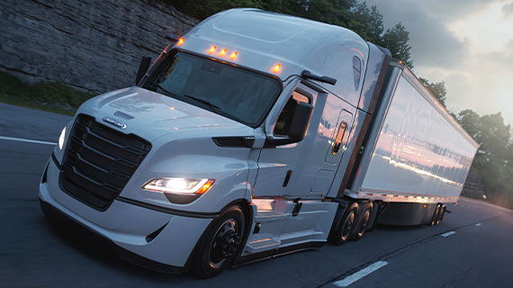 Modern Cascadia semi truck with white trailer illuminated at dusk, LED headlights and marker lights glowing