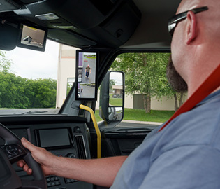 Freightliner truck cab interior view with driver operating steering wheel and digital dashboard display